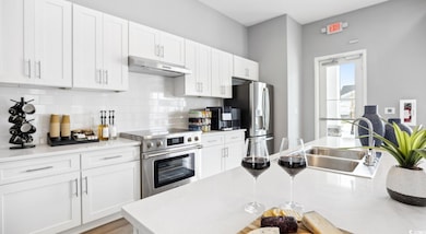 Kitchen with appliances with stainless steel finishes, under cabinet range hood, white cabinets, light countertops, and decorative backsplash