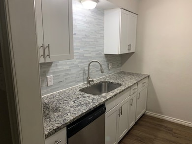 Kitchen featuring tasteful backsplash, white cabinetry, stainless steel dishwasher, light stone counters, and dark wood-style floors