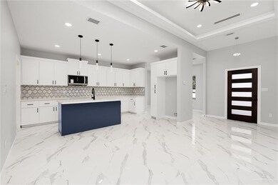 Kitchen featuring pendant lighting, backsplash, white cabinetry, and an island with sink