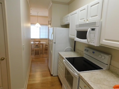 Kitchen with white appliances, white cabinetry, light wood finished floors, light countertops, and crown molding