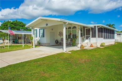 Rear view of house featuring concrete driveway, a yard, an attached carport, a sunroom, and a patio