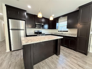 Kitchen with stainless steel appliances, wood tiled floors, a kitchen island, light stone countertops, and pendant lighting