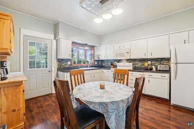 Kitchen with white appliances, dark wood finished floors, backsplash, white cabinets, and crown molding