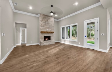 Unfurnished living room with a stone fireplace, wood finished floors, crown molding, recessed lighting, and ceiling fan