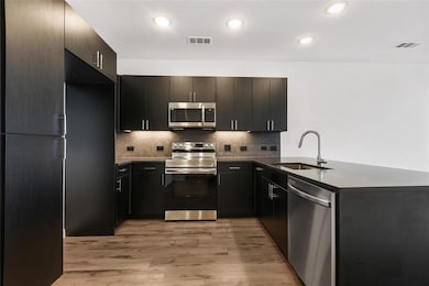 Kitchen featuring appliances with stainless steel finishes, backsplash, a peninsula, light wood-style flooring, and dark stone countertops