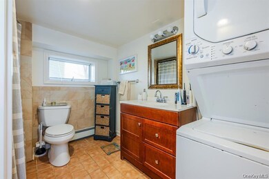 Bathroom featuring stacked washer and clothes dryer, light tile patterned flooring, vanity, a baseboard radiator, and a shower with curtain