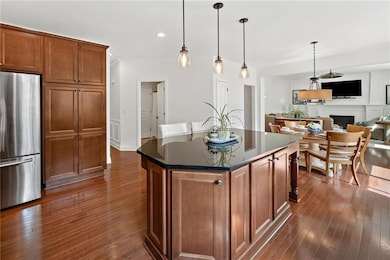 Kitchen featuring freestanding refrigerator, dark wood-style flooring, brown cabinets, a fireplace, and recessed lighting