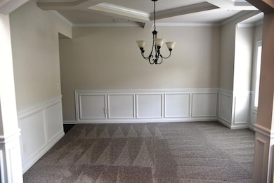Unfurnished dining area featuring dark carpet, a decorative wall, a chandelier, crown molding, and a wainscoted wall