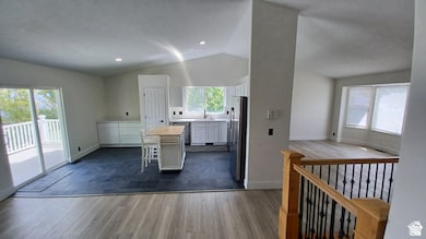 Kitchen featuring white cabinetry, dark wood-type flooring, a kitchen island, vaulted ceiling, and stainless steel appliances