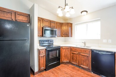 Kitchen with black appliances, brown cabinets, light countertops, hanging light fixtures, and light wood finished floors