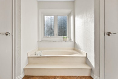 Full bath featuring a garden tub, a textured wall, and tile patterned floors