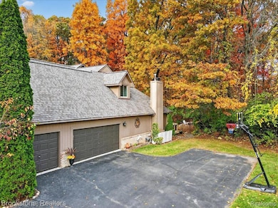 View of front of home with a chimney, driveway, roof with shingles, and a front lawn