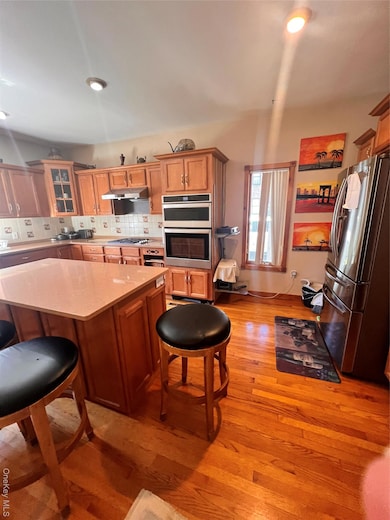 Kitchen featuring a breakfast bar area, backsplash, stainless steel appliances, light wood-type flooring, and glass insert cabinets