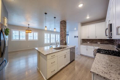 Kitchen with white cabinets, tasteful backsplash, an island with sink, stainless steel appliances looking toward spacious family room with lots of amazing windows.
