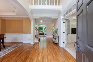 Welcoming two-story foyer with gleaming hardwood floors, elegant trim detail, and open views to the formal dining room, private office, and sunlit living area.