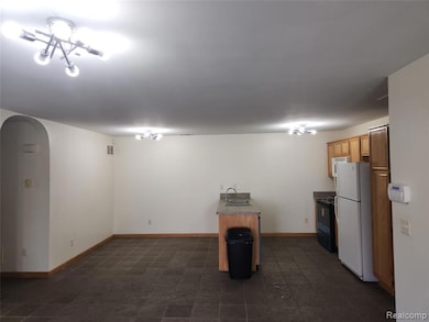 Kitchen featuring arched walkways, freestanding refrigerator, black stove, dark countertops, and brown cabinets