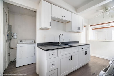 Kitchen with washer / dryer, white cabinets, dark wood-style floors, electric panel, and ceiling fan