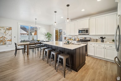 Kitchen featuring white cabinets, appliances with stainless steel finishes, a breakfast bar, a kitchen island with sink, and recessed lighting