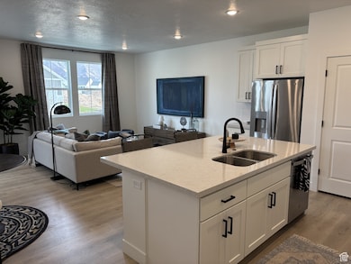 Kitchen with white cabinetry, open floor plan, appliances with stainless steel finishes, a center island with sink, and light wood finished floors