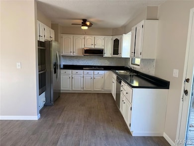 Kitchen featuring dark countertops, white cabinetry, stainless steel appliances, dark wood-style floors, and backsplash