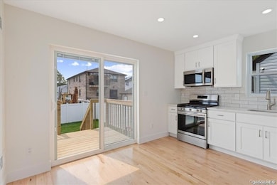 Kitchen featuring appliances with stainless steel finishes, white cabinetry, recessed lighting, backsplash, and light wood finished floors