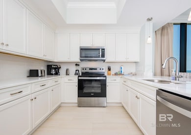 Kitchen featuring appliances with stainless steel finishes, hanging light fixtures, white cabinets, light stone counters, and crown molding