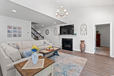 Living area featuring wood finished floors, a chandelier, stairs, a glass covered fireplace, and recessed lighting