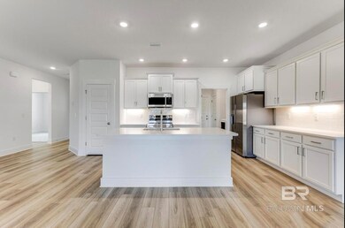 Kitchen featuring white cabinetry, light hardwood / wood-style floors, appliances with stainless steel finishes, backsplash, and a kitchen island with sink