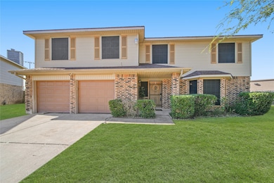 This two-story home features a brick facade with a double garage and a welcoming front porch. It is set on a well-maintained lawn with neatly trimmed shrubs, offering great curb appeal.