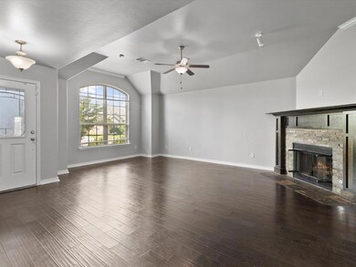 Unfurnished living room with vaulted ceiling, a ceiling fan, wood finished floors, and a stone fireplace