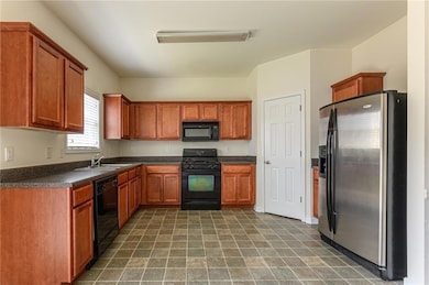 Kitchen featuring black appliances, dark countertops, a sink, and brown cabinetry