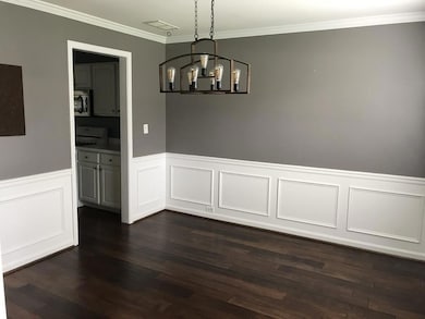 Unfurnished dining area featuring ornamental molding, wainscoting, dark wood-style floors, a chandelier, and a decorative wall