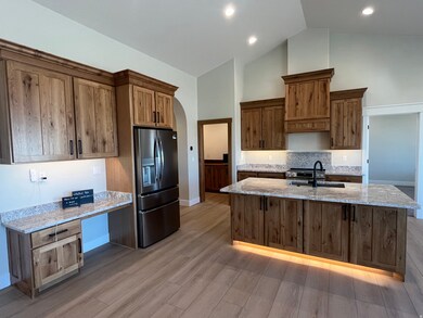 Kitchen with light stone counters, stainless steel appliances, high vaulted ceiling, an island with sink, and brown cabinetry