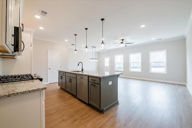 MODEL REPRESENTATIVE- Kitchen with crown molding, light stone countertops, pendant lighting, light wood-type flooring, and a center island with sink
