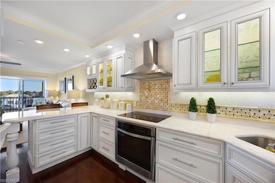 Kitchen with white cabinets, ornamental molding, glass insert cabinets, stainless steel oven, and wall chimney range hood