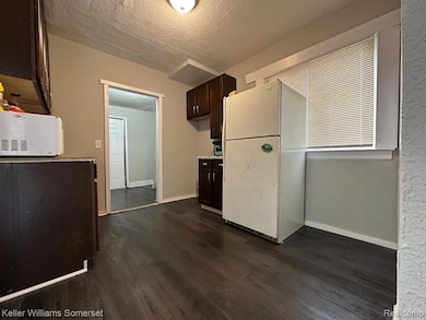 Kitchen featuring dark brown cabinetry, a textured ceiling, white appliances, light countertops, and dark wood finished floors