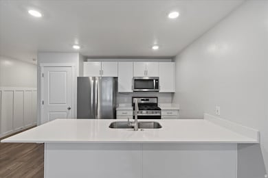 Kitchen with stainless steel appliances, white cabinets, a peninsula, light stone countertops, and recessed lighting