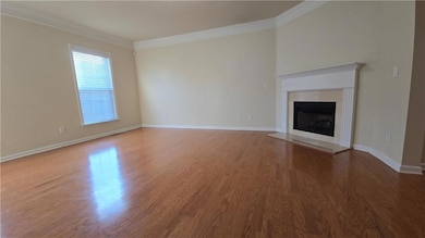Unfurnished living room featuring arched walkways, crown molding, wood finished floors, a fireplace with flush hearth, and baseboards