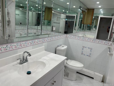 Bathroom featuring light tile patterned floors, baseboard heating, tile walls, vanity, and tasteful backsplash