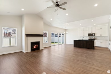Unfurnished living room featuring vaulted ceiling, ceiling fan, light wood-style flooring, recessed lighting, and a lit fireplace