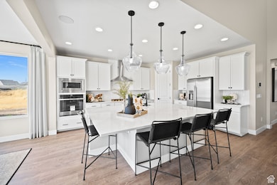 Kitchen with a breakfast bar area, stainless steel appliances, a large island, white cabinets, and decorative light fixtures