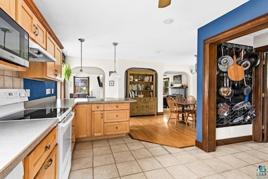 Kitchen with white range with electric stovetop, stainless steel microwave, arched walkways, a peninsula, and light tile patterned flooring