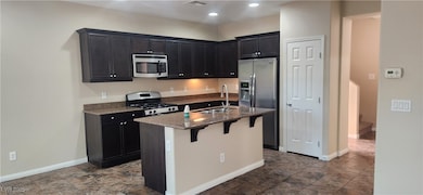 Kitchen with stainless steel appliances, dark stone counters, a breakfast bar area, dark cabinetry, and recessed lighting