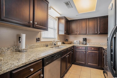 Kitchen with dark brown cabinetry, light stone counters, appliances with stainless steel finishes, and light tile patterned floors