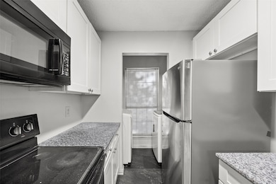 Kitchen featuring black appliances, white cabinetry, a textured ceiling, washer / clothes dryer, and light stone countertops