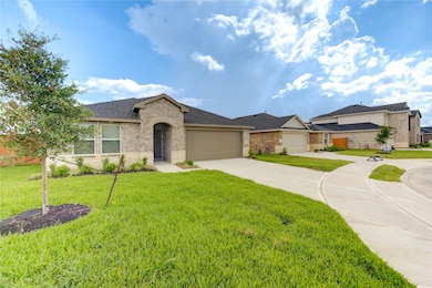 This photo showcases a modern single-story brick home with a two-car garage, well-maintained lawn, and a young tree in the front yard, situated in a suburban neighborhood under a partly cloudy sky.