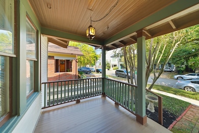 This photo showcases a charming front porch with a wooden ceiling and railings, providing a cozy outdoor space. Looking at a tree-lined street, offering a welcoming and peaceful atmosphere.