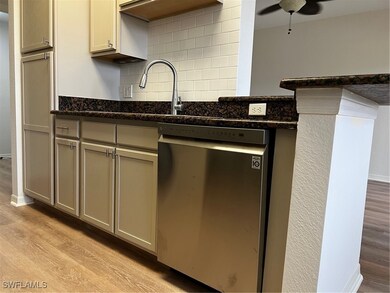 Kitchen featuring dishwashing machine, light wood finished floors, tasteful backsplash, a ceiling fan, and dark stone counters