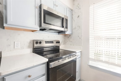 Kitchen featuring appliances with stainless steel finishes, tasteful backsplash, light stone countertops, and white cabinetry