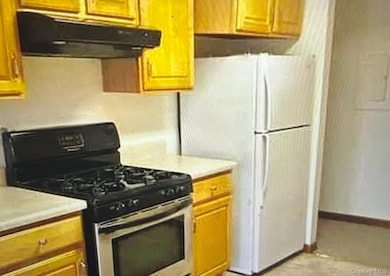 Kitchen featuring stainless steel range with gas cooktop, under cabinet range hood, light countertops, and brown cabinetry